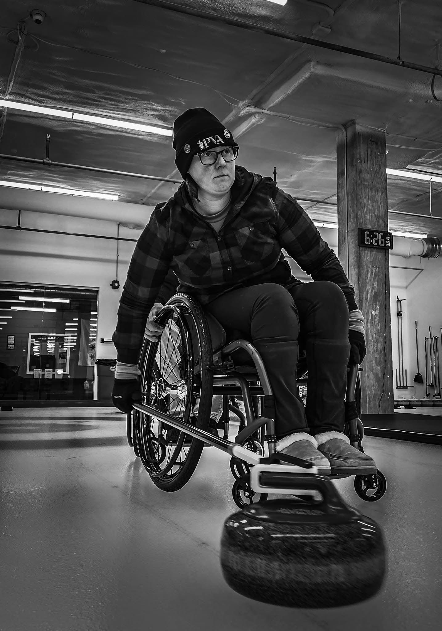 Person in a wheelchair with curling broom in an indoor setting